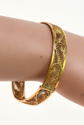 une image montrant un gros plan du bras d'une personne portant un bracelet en or