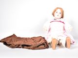 a doll sitting next to a blanket on a white surface