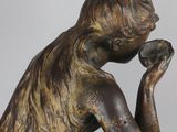 an antique bronze statue of a woman sitting on a rock