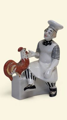 une figurine représentant une femme assise sur un banc avec un coq