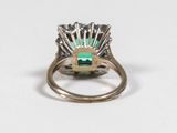 a close up of an emerald and diamond ring on a white surface