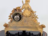 a gold clock with a woman sitting on top of it