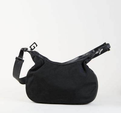 le sac noir est posé sur une surface blanche et est muni d'une bandoulière noire