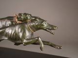 a bronze sculpture of two greyhounds running on a black surface