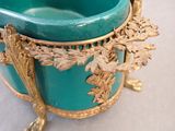 a green and gold vase on a white table