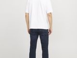 a man standing in front of a white wall wearing a white t - shirt and blue jeans