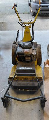 a lawn mower sitting on the sidewalk next to a car