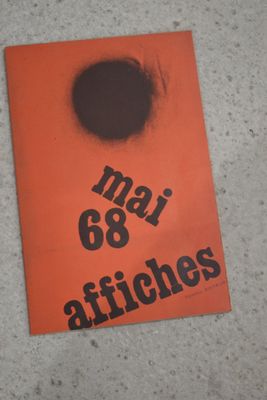 un livre orange avec un point noir dessus, posé par terre