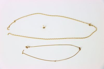 deux colliers en or et un bracelet posés sur une surface blanche