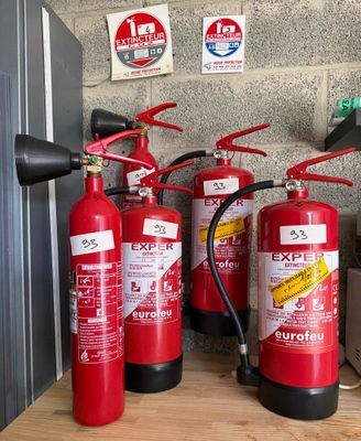 Plusieurs extincteurs sont alignés contre un mur de briques