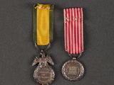two medals on a black surface with a red, white, and yellow ribbon