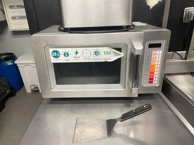 a silver microwave sitting on a counter with a spatula in front of it