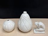 three white vases sitting on a table next to a small figurine