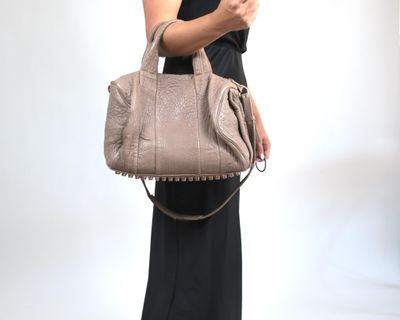 une femme en robe noire, tenant un sac à main beige et regardant son téléphone portable
