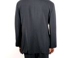 the back of a man in a black suit standing in front of a white wall