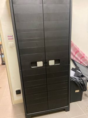 une armoire noire à deux portes et un sac noir posé par terre