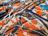 an orange, blue, and black rug with paint splatters on it