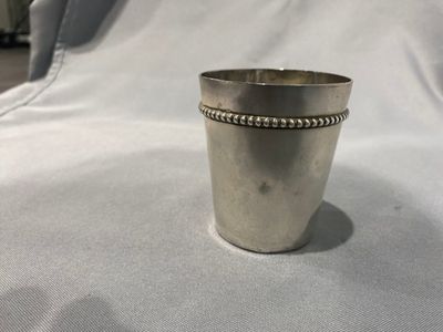une vieille coupe en argent au bord perlé repose sur un lit