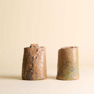 une paire de salières et poivrières en céramique marron posées sur une surface blanche