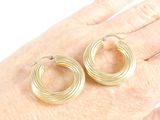 a woman ' s hand holding a pair of gold hoop earrings