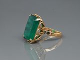 an image of a ring with a green stone on a reflective surface