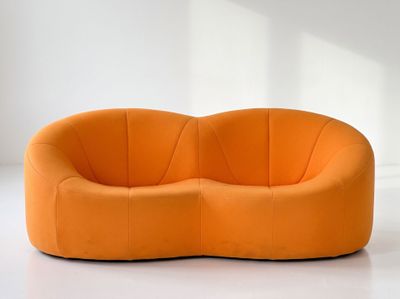 an orange curved sofa sitting on top of a white floor next to a window
