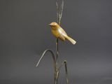 sculpture of a yellow bird sitting on top of a tall plant