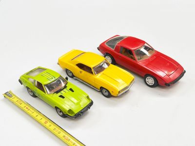 trois petites voitures posées à côté d'une règle sur une surface blanche
