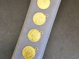 trois pièces d'or sont posées sur un tissu bleu, retenues par un cordon argenté