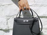 someone is holding a black handbag in front of a white brick wall