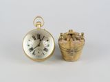 une petite montre de poche en or à côté d'un petit panier en or