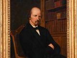 portrait of a man in a black suit and bow tie sitting in a chair