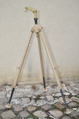 a wooden tripod on a stone floor next to a white wall