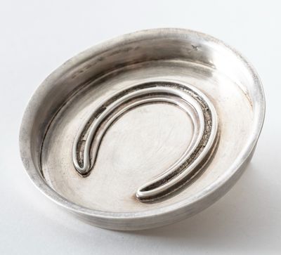 a silver bowl with a horseshoe on it on a white surface