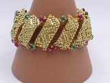 gold plated bracelet with multi colored stones on top of a brown vase