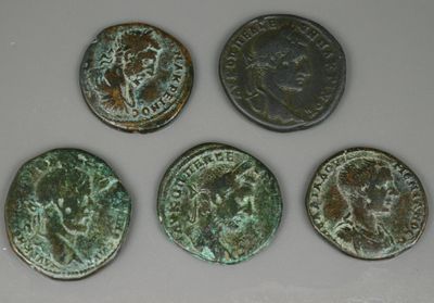 Quatre pièces de monnaie romaines antiques sont disposées en rangée sur une surface blanche