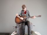 a figurine of a man sitting on a rock playing a guitar