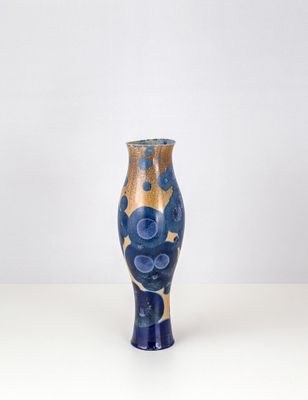 un vase bleu et or posé sur une surface blanche