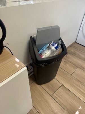 une poubelle noire posée à côté d'un lave-linge et d'un sèche-linge dans une salle de bains