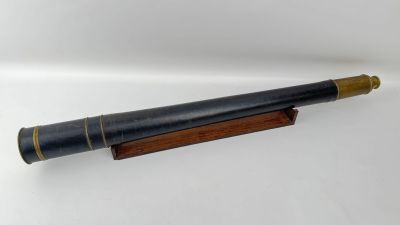 un vieux télescope posé sur un socle en bois, sur une surface blanche