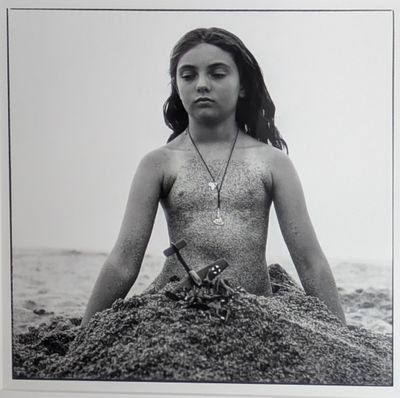photographie en noir et blanc d'une femme assise sur le sable, à la plage