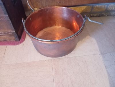 un grand chaudron en cuivre posé par terre à côté d'une porte en bois
