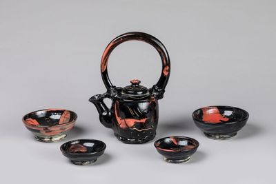 three black and red bowls and a teapot on a table
