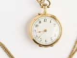 une image représentant une montre de poche en or avec une chaîne, posée sur une surface blanche