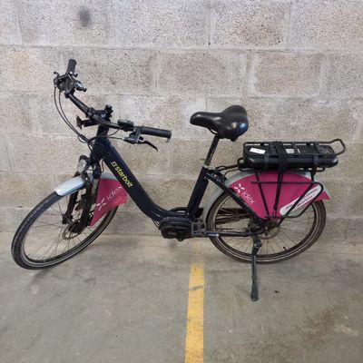 un vélo rose garé sur un parking, près d'un mur