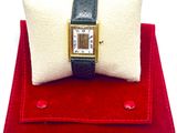 une petite montre carrée posée sur un coussin rouge, à côté d'un oreiller blanc
