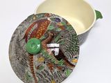 a bird on the lid of a bowl on a white surface