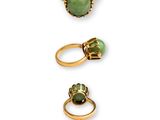 three gold rings with green stones on a white background