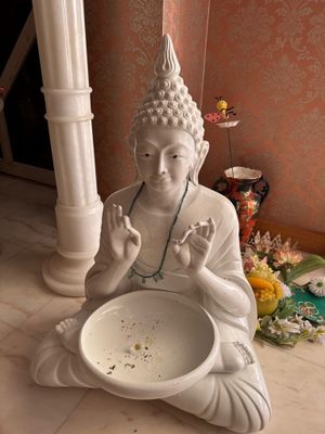 une statue de Bouddha assis par terre, avec un bol de nourriture devant lui