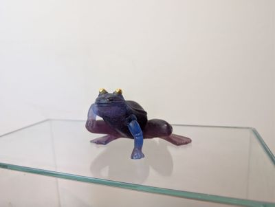 purple frog figurine sitting on top of a glass shelf